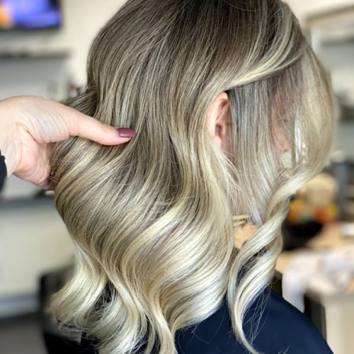 A hand showcasing wavy blonde hair with soft curls in a salon setting.